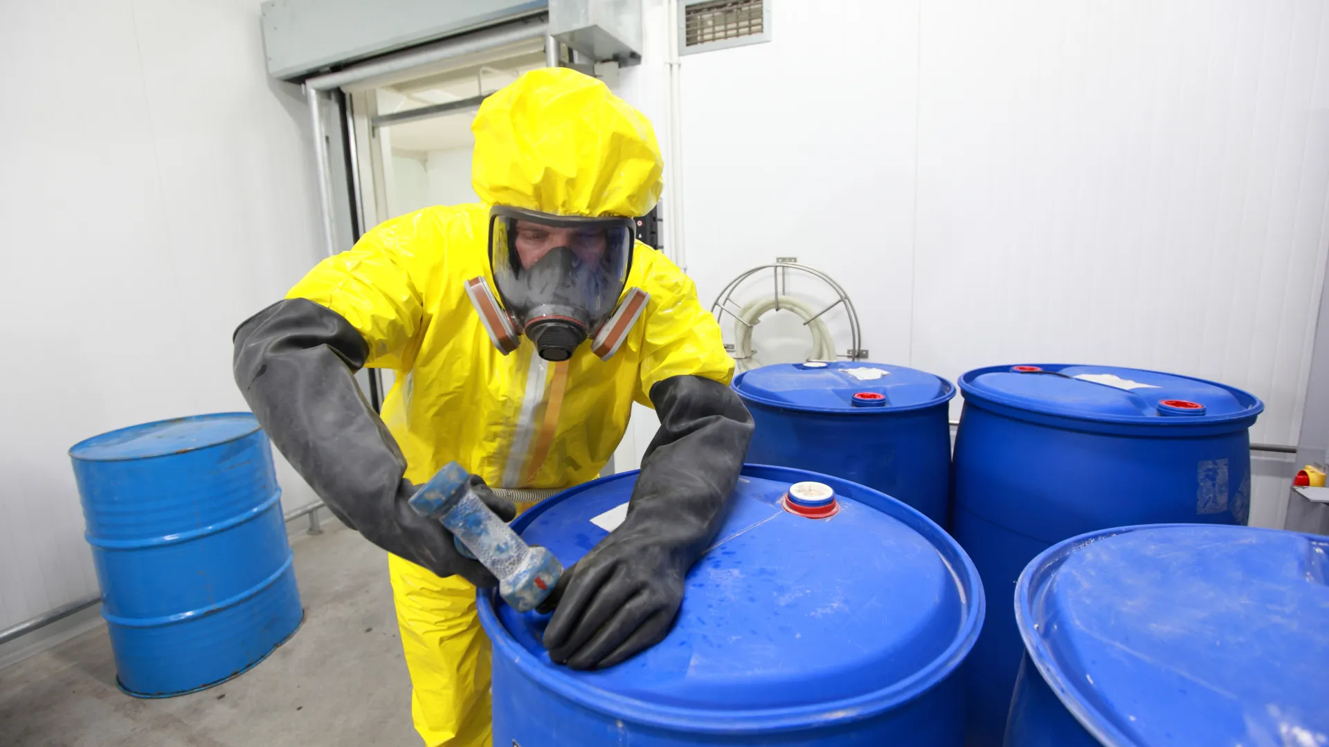 Arbeiter im Schutzanzug und blaue Plastikfässer